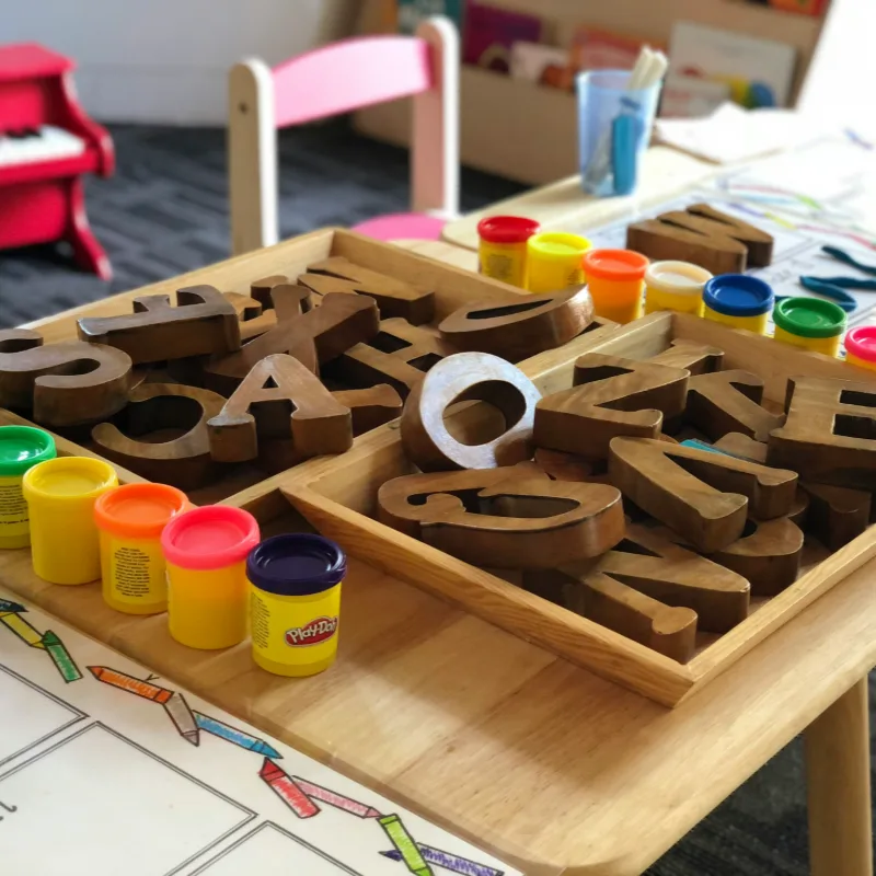 Wooden alphabet letters and cups of Play-Doh laid out on a craft table.