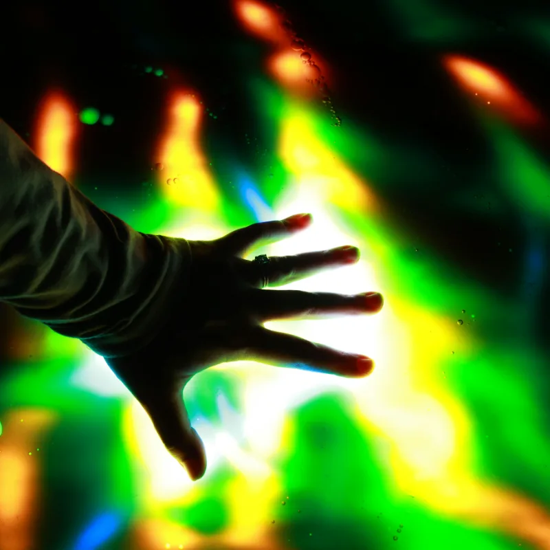 A hand reaches toward a wall of colorful sensory lights.
