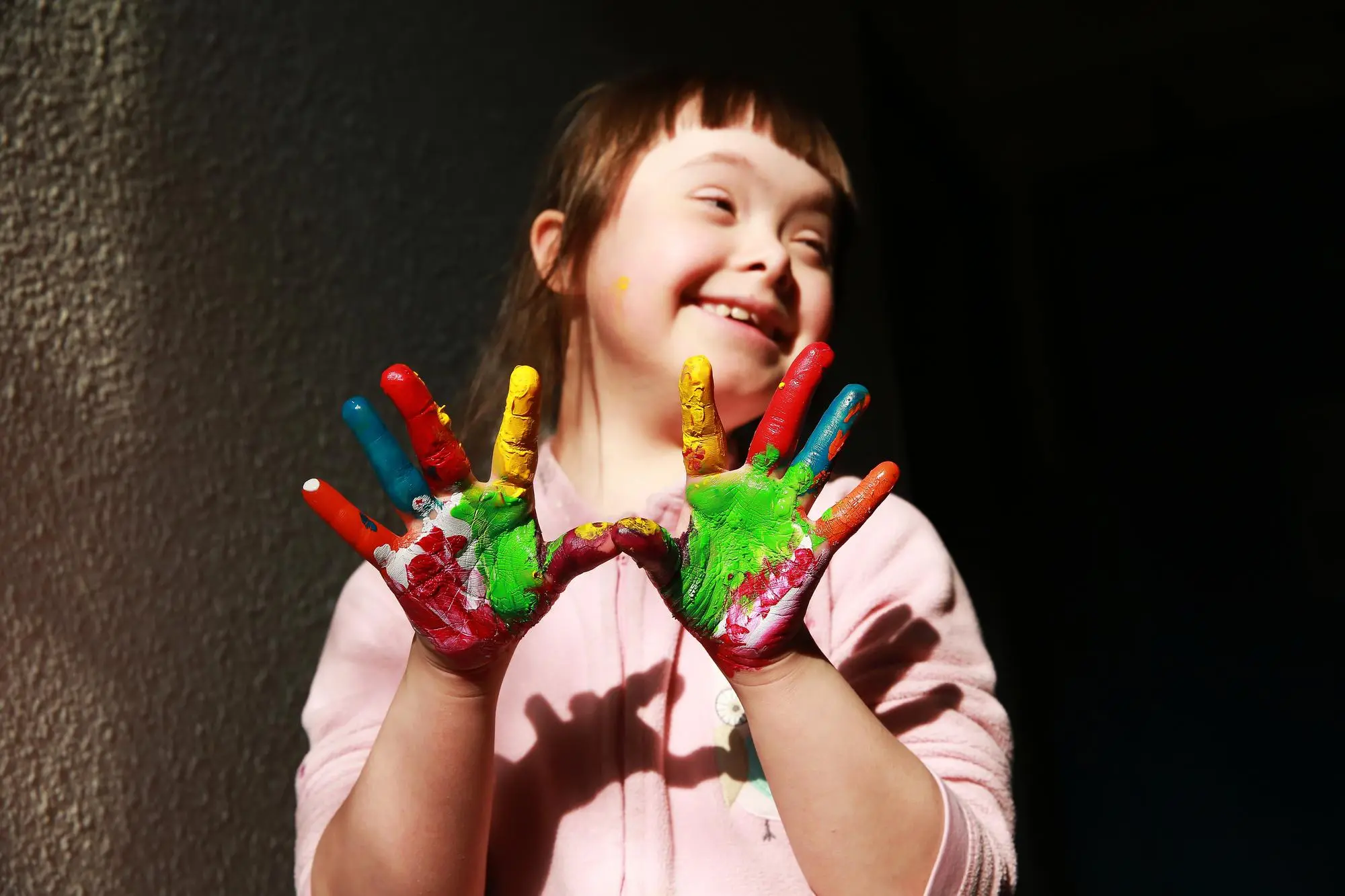 A girl smiles wide, holding up both hands covered in bright finger paint.